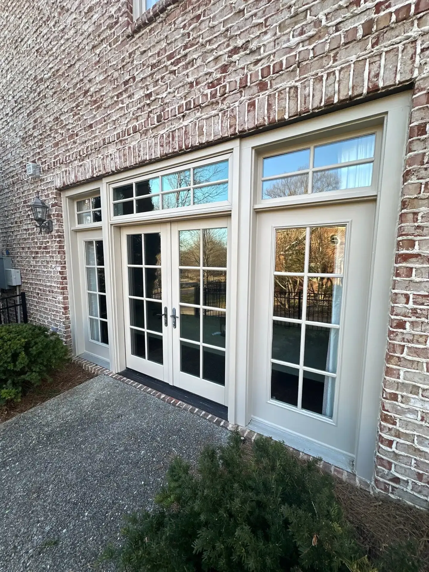 Exterior view of white-framed glass doors and windows set into a brick wall. A small garden is in the foreground.