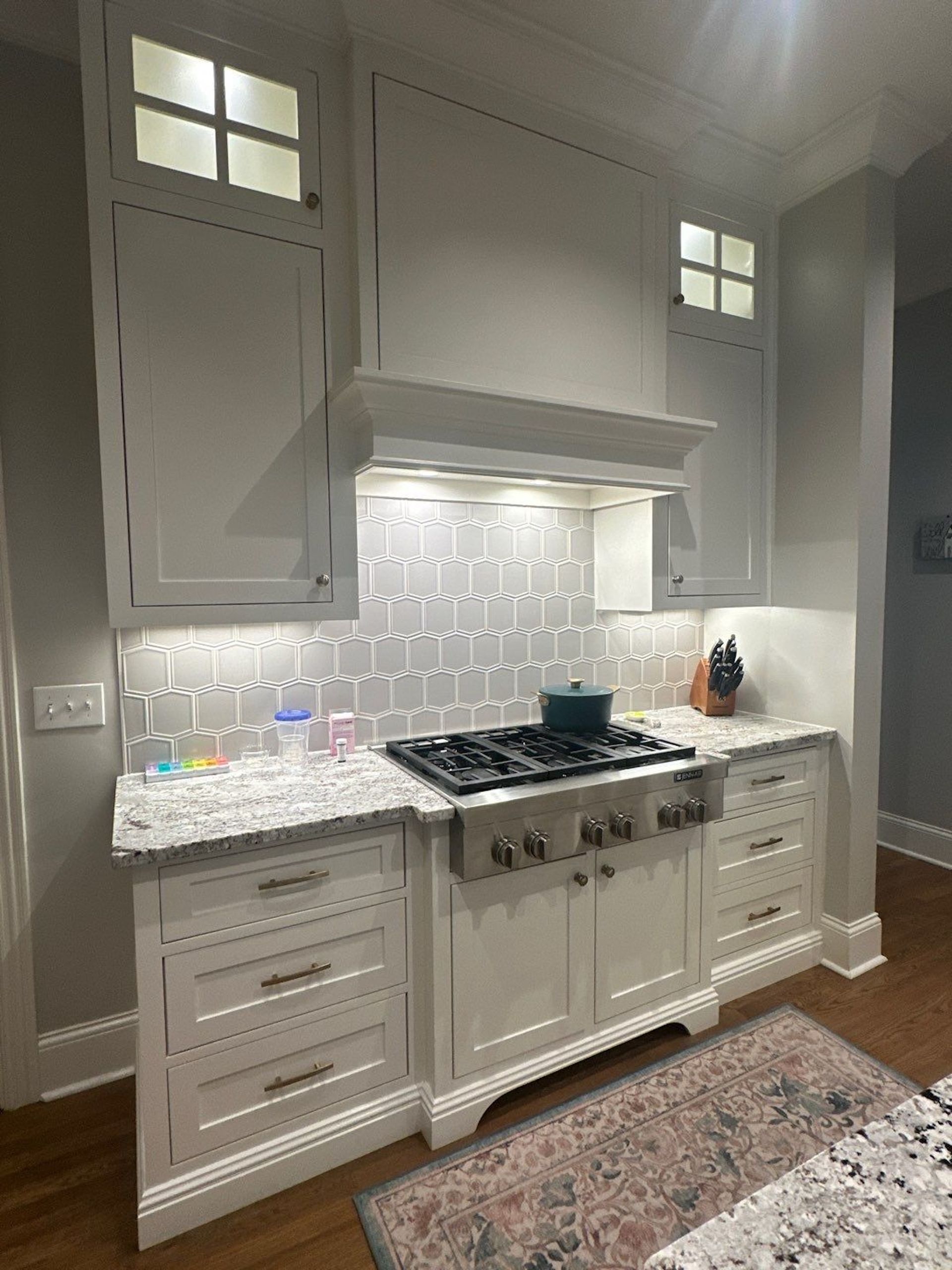 White kitchen with a stove, hood, cabinets, and a granite countertop.