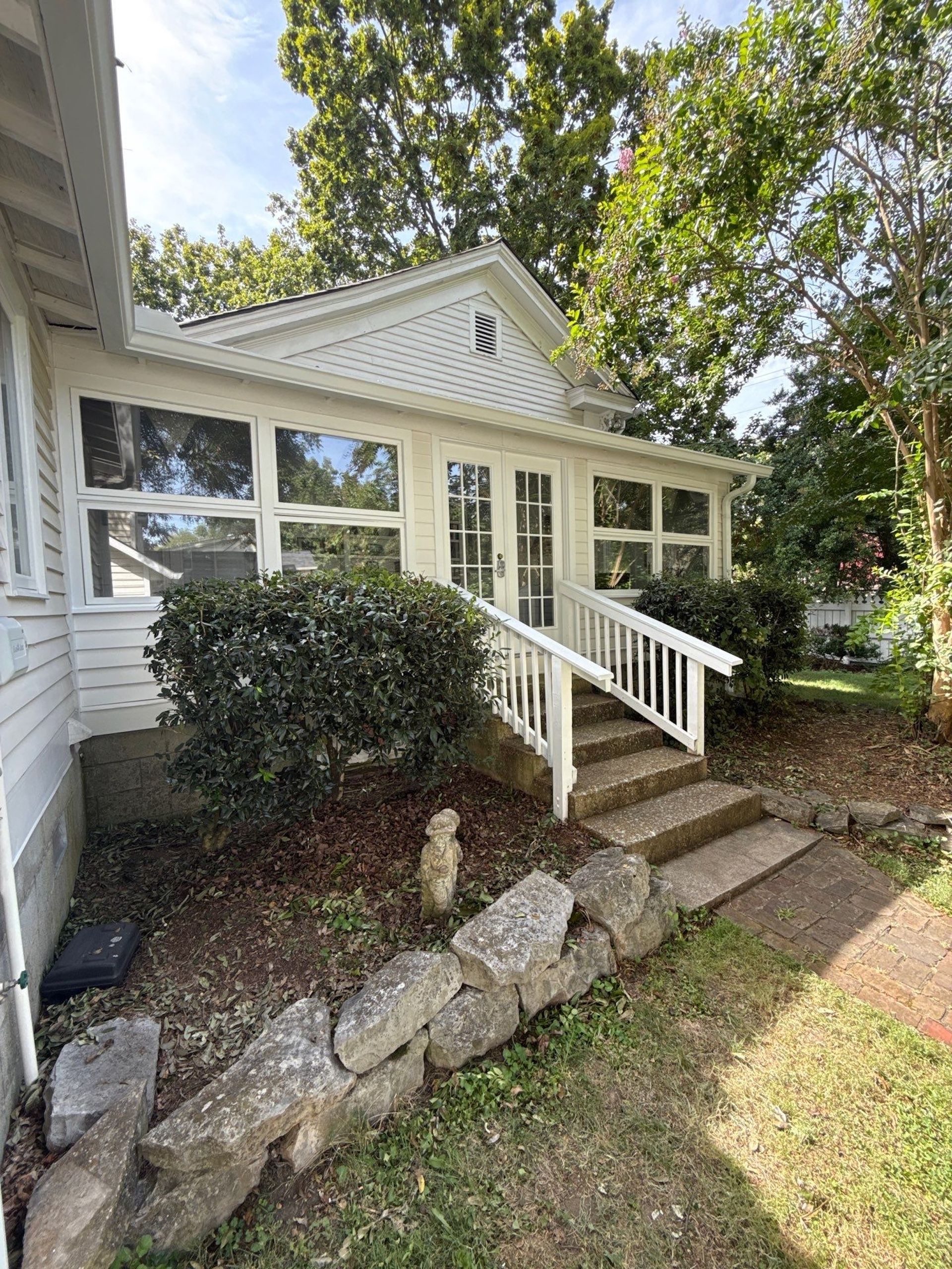 White porch with large windows and a small staircase. A stone wall borders the front yard.