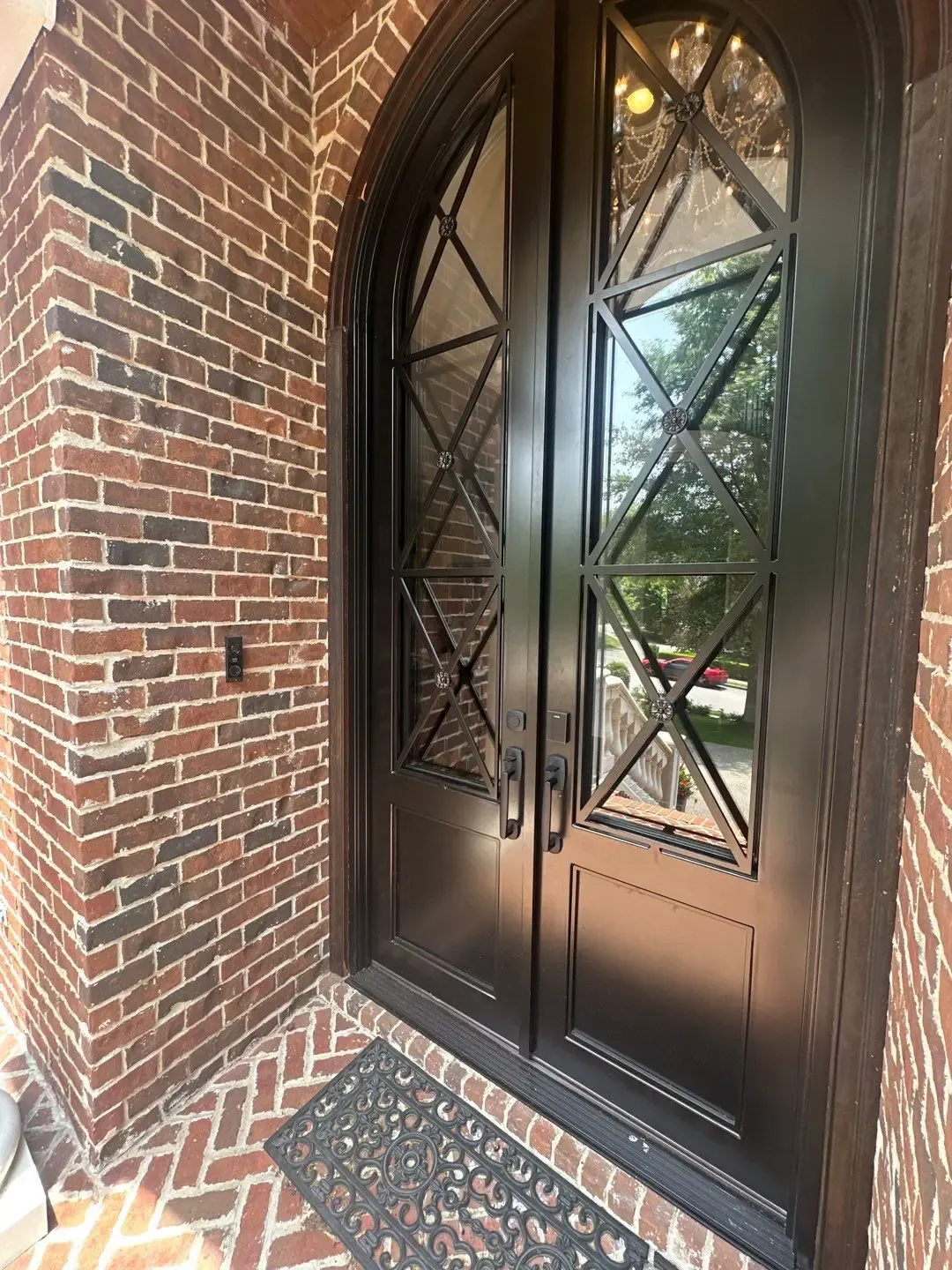 Black arched double doors with decorative glass panels and metalwork, set in a brick entryway.